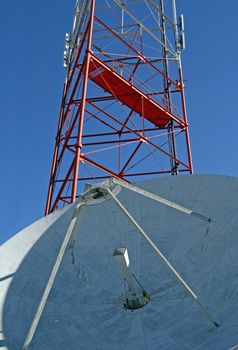 A satellite dish and radio tower on a clear blue sky.