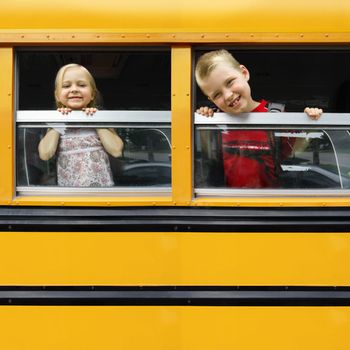 Photo of two happy children looking out the windows of a yellow school bus. Plenty of space for text.