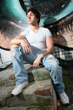 young man sits on concrete steps on background of the graffiti