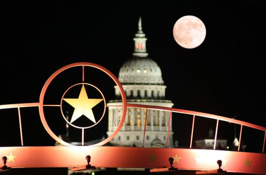 A shot of the star of Texas with the Texas State Capitol Building and the moon in the background.