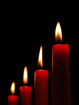 Four burning red candles on black background.