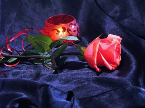 Red rose and candle on the dark-blue satin