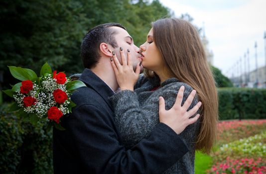 Young Couple Kissing in park with roses bouquet