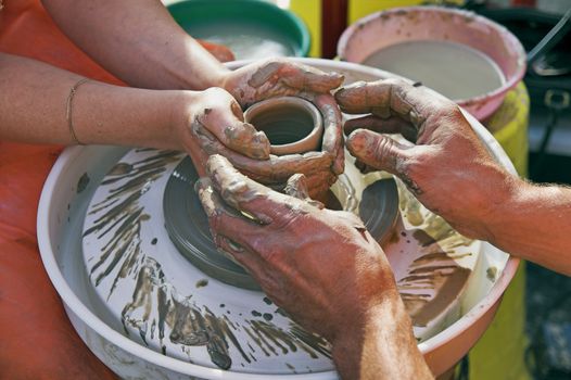 potter's hands guiding woman's hands to help her learn pottery