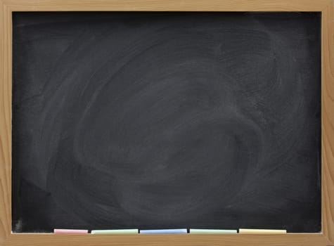 blank blackboard in wooden frame, colorful chalk sticks, and eraser smudges