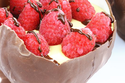 Edible chocolate bowl filled with vanilla pudding, topped with fresh red raspberries and drizzled with chocolate.