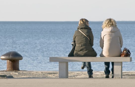 Two fiends talking, sitting on a bench in front of the sea