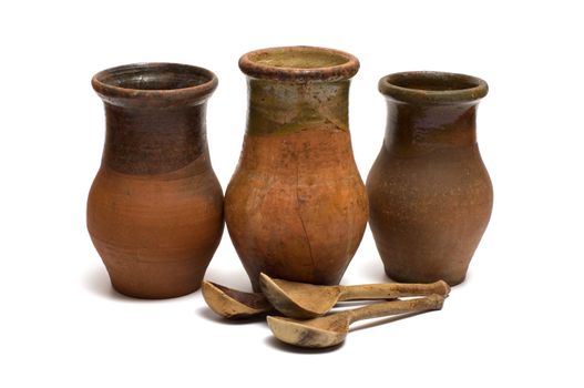 Three old earthenware crock and three wooden spoons on a white background.