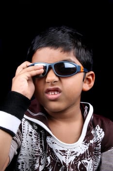A cute Indian boy wearing sunglasses, on black studio background.