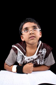 A little Indian boy lost in his dreams while doing his homework studies, on black studio background.