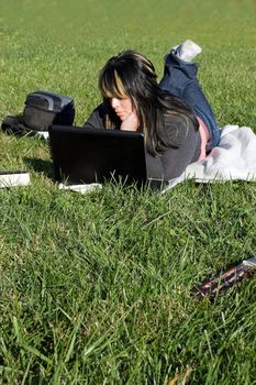 A young student using her laptop computer while laying in the grass on a nice day.