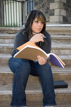 A young woman holding her notebook while sitting on the campus stairs.