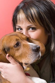 A pretty young hispanic woman kissing her beagle puppy.