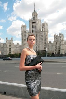 serious beautiful girl in black-silvery dress on background of the old moscow skyscraper