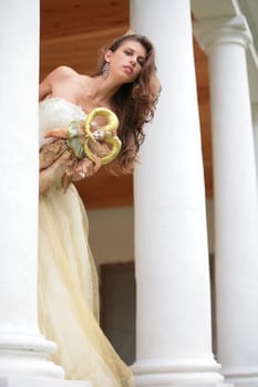 beautiful girl in gown of the bride with doll peers out from behind pillar