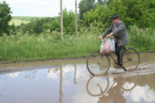 The farmer on a bicycle comes back home after work in the Kharkov area passing through rain lake 15.06.2006
