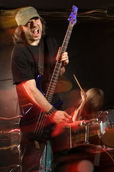 Bass player playing on a stage with female drummer. Shot with strobes and slow shutter speed to create lighting atmosphere and blur effects. Motion blur on performers.