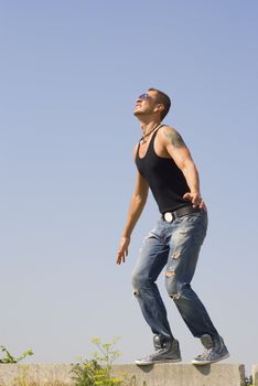 Expressive man strained pose with opend arms stays in protextive poze. He wears sun glasses and has tatoo on  the left shoulder. Tattoo represent the person in a hood.