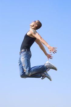 The young athletic man flies to the sun with open arms. There is a tattoo on his hand and sun reflection in glasses.