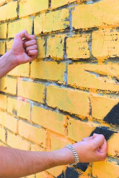 Fists of the young man are touching the wall. There is a silver bracelet on right arm.