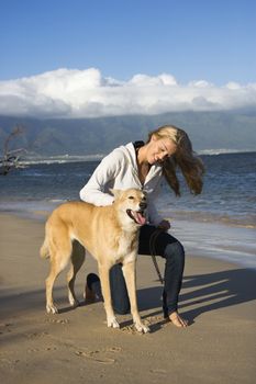 Caucasian woman petting brown dog on leash on Maui, Hawaii beach.