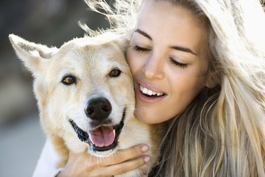 Pretty Caucasian blond woman hugging brown dog and smiling.