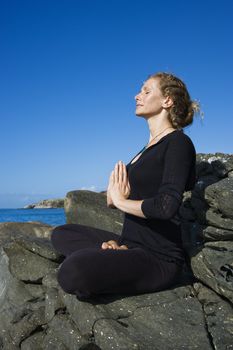 Caucasian mid-adult woman practicing yoga on rocky coast of Maui, Hawaii.