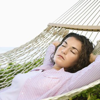 Pretty young adult Caucasian brunette female lying in hammock with arms behind head sleeping.