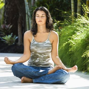 Pretty young adult Caucasian brunette woman sitting in lotus position practicing yoga.