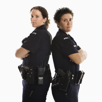 Portrait of two mid adult Caucasian policewomen standing back to back looking over their shoulders smiling at viewer.