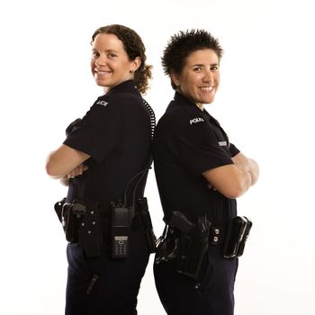 Portrait of two mid adult Caucasian policewomen standing back to back looking over their shoulders and smiling at viewer.