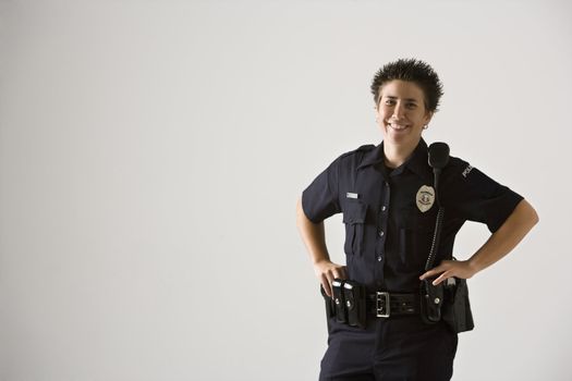 Portrait of mid adult Caucasian policewoman standing with hands on gun holster looking at viewer smiling.