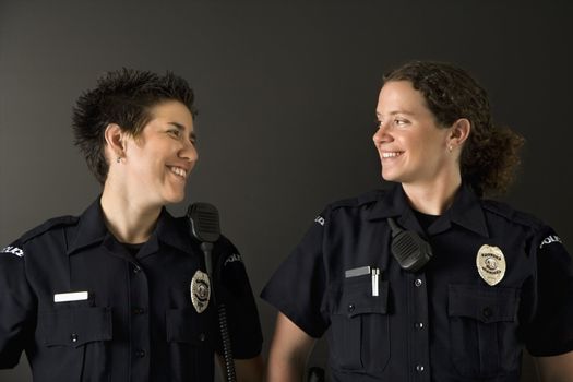Two mid adult Caucasian policewomen standing looking at each other smiling.