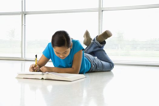 Asian preteen girl lying on floor doing homework.