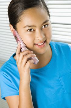 Asian preteen girl talking on cell phone and looking at viewer.