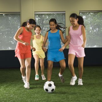 Four multiethnic girls playing soccer and laughing in indoor gym.