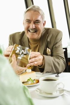 Mature Caucasian couple having dinner in nice restaurant as man gives gift to woman.