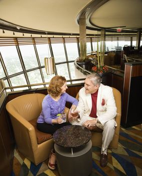 Mature Caucasian couple sitting in bar lounge having drinks and talking.