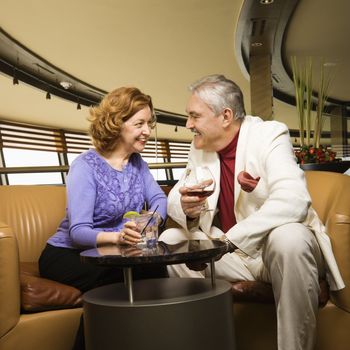Mature Caucasian couple sitting in bar lounge having drinks and talking.