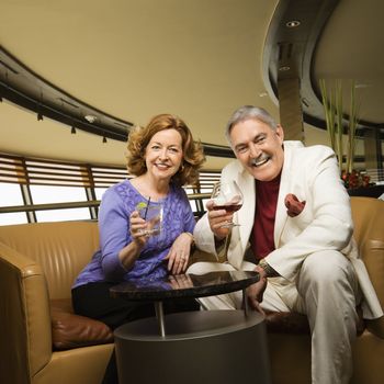 Mature Caucasian couple sitting in bar lounge having drinks and smiling.