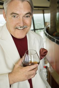 Mature Caucasian man in suit holding snifter of brandy smiling.