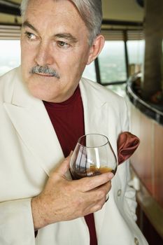 Mature Caucasian man in suit holding snifter of brandy.