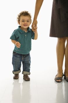 African American toddler boy holding onto mothers hand smiling at viewer.