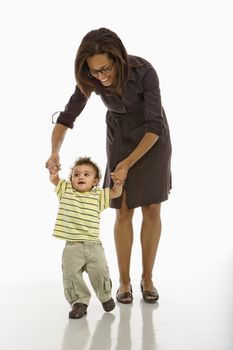 African American mid adult mother holding arms of toddler son learning to walk.
