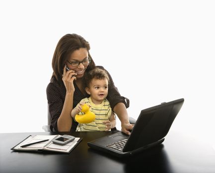 African American mid adult businesswoman working on laptop and cell phone with toddler son on lap.