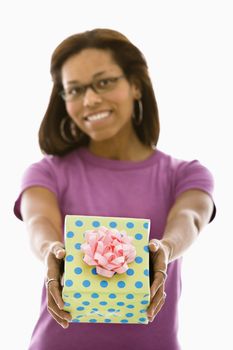 African American mid adult woman holding wrapped package out towards viewer.