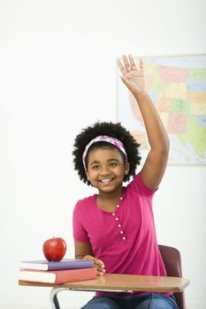 African American girl sitting in school desk raising hand and smiling at viewer.