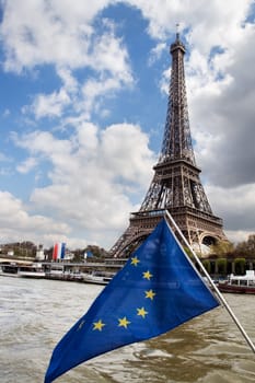 View at Eiffel tower across the Seine River from boat. European Union flag in front.