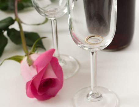 A soft focus view of a ring in a wine glass, with a pink rose