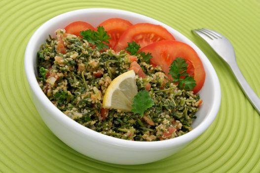 Tabbouleh with tomato slices in a white bowl, ready to eat